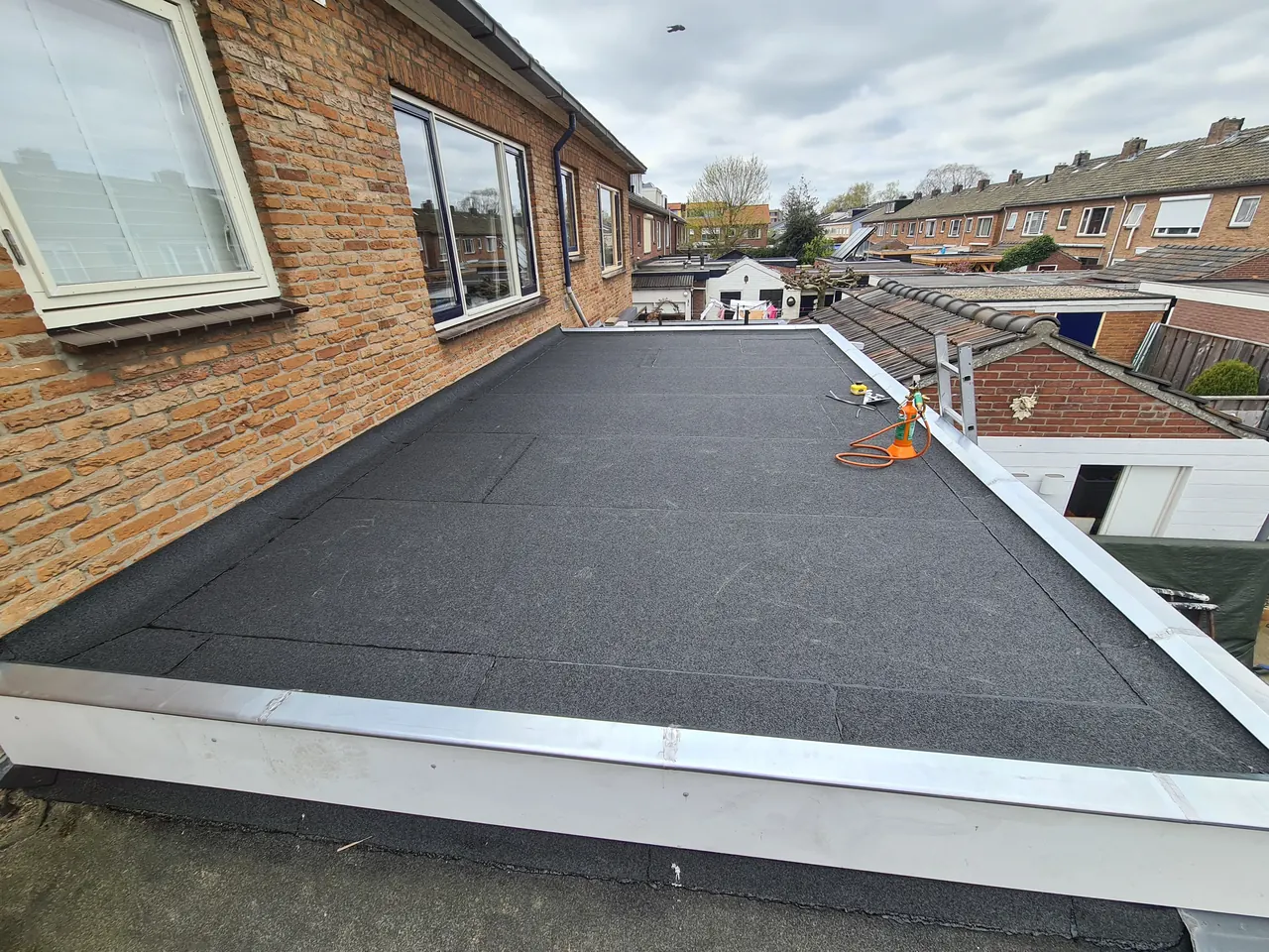 Nieuw bitumen dak met randafwerking langs een gevel in Harderwijk